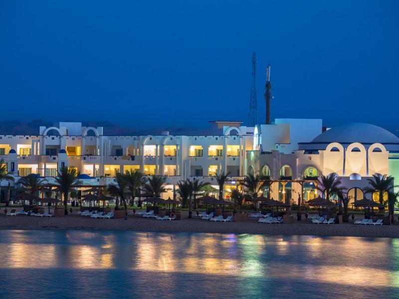 Hotel sull'acqua con balconi illuminati e palme di notte