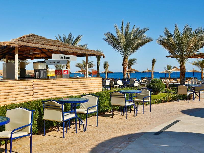 Bar sulla spiaggia con sedie, tavoli e palme sotto un cielo azzurro e mare