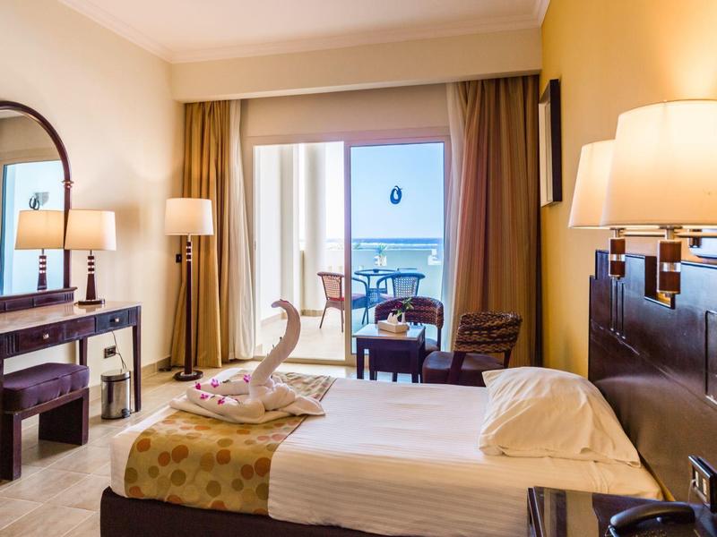 Camera d'hotel accogliente con letto matrimoniale, scrivania, sedie e balcone con vista mare.