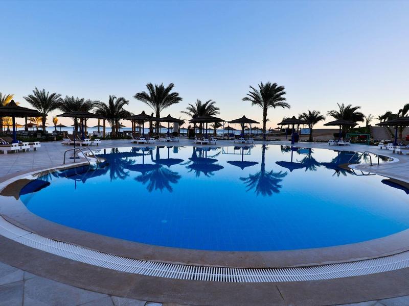 Piscina rotonda dell'hotel con palme e lettini sullo sfondo al tramonto.