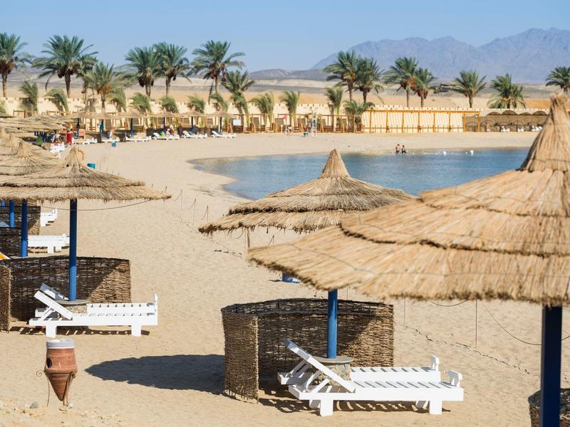 Spiaggia con capanne di paglia, lettini e palme davanti a una catena montuosa