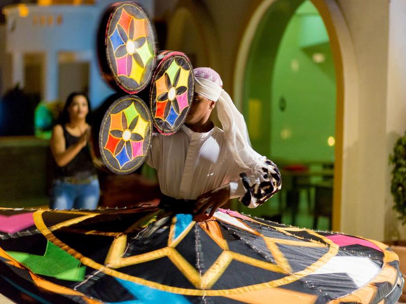 Danzatore tradizionale indossa un costume colorato con motivo geometrico al coperto.