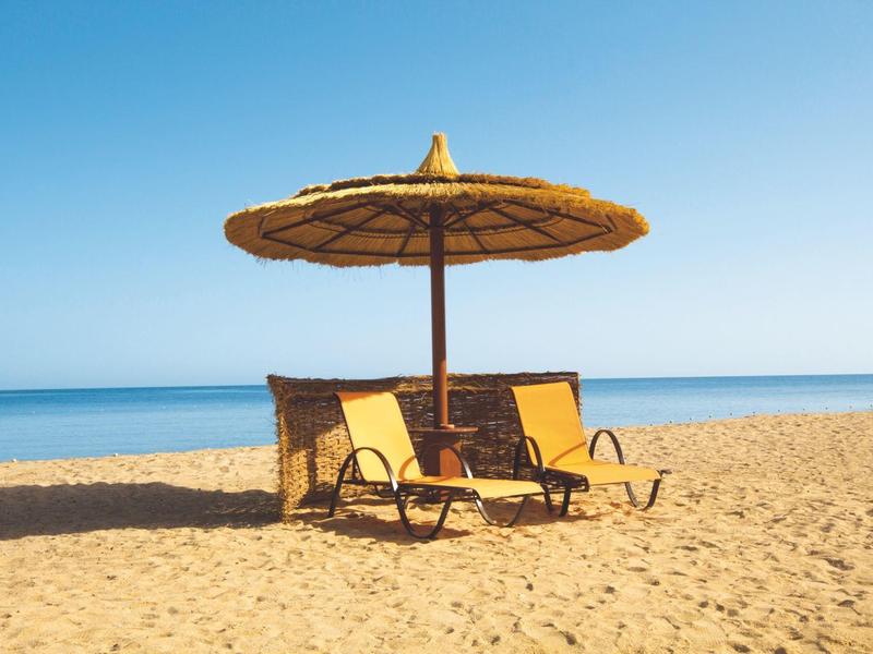 Due sdraio sotto un ombrellone di paglia sulla spiaggia con vista sul mare.