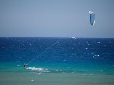 Person kite surfing on calm sea under blue sky