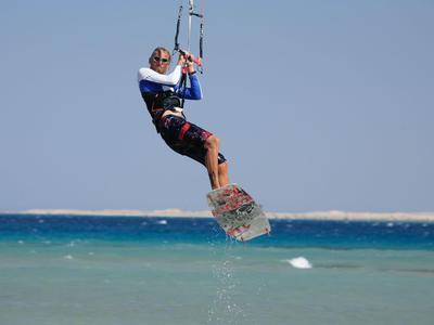 A man jumps with a kiteboard over the sea under a clear sky.