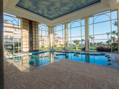 Indoor swimming pool with large windows offering views of outdoor area with palm trees.