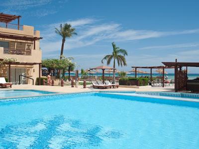 Large blue swimming pool with lounge chairs and palm trees under a blue sky at a seaside resort.