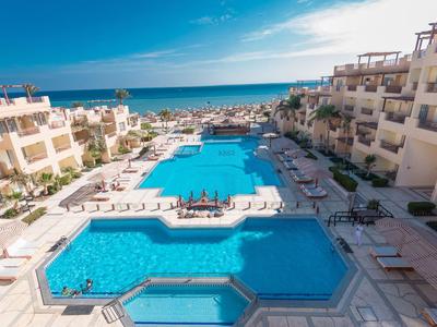 Large hotel pool with lounge chairs and sea view under a blue sky.