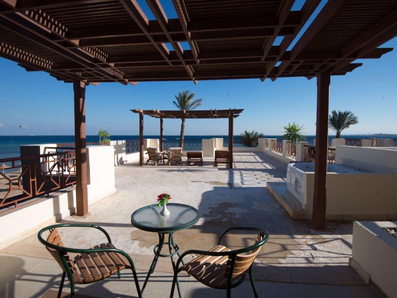 Zonnig terras met zithoek en uitzicht op zee onder een houten pergola.