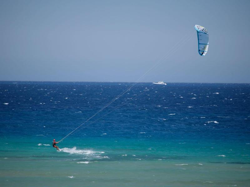 Kitesurfer glijdt over turquoise water onder een heldere hemel.