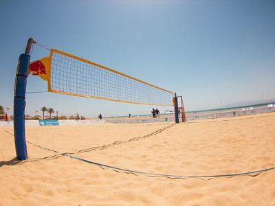 Volleyballnetz am Sandstrand, blauer Himmel und Meeresufer im Hintergrund an einem sonnigen Tag.
