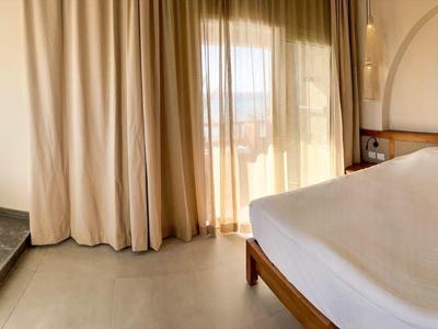 Helles Hotelzimmer mit großem Bett, Balkon, Vorhängen und Tisch mit Snacks und Getränken.