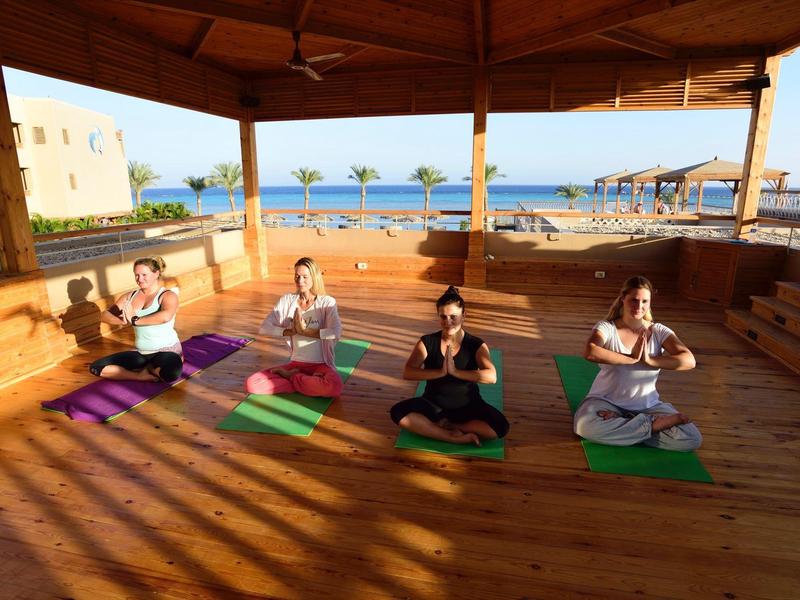 Vier Personen machen Yoga auf einer Holzterrasse mit Meerblick am Hotel