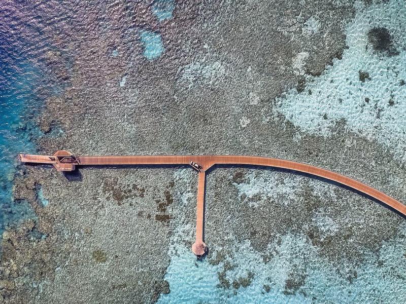 Langer, roter Pier erstreckt sich über klares, türkisfarbenes Wasser mit Korallenriff darunter.
