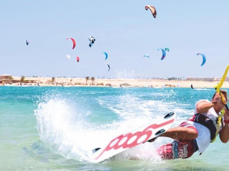 Kitesurfer bei starkem Wind auf dem Meer mit blauem Himmel und mehreren Kites im Hintergrund.