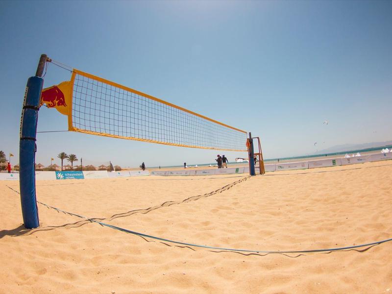Volleyballnetz am Strand mit Menschen und blauem Himmel im Hintergrund.