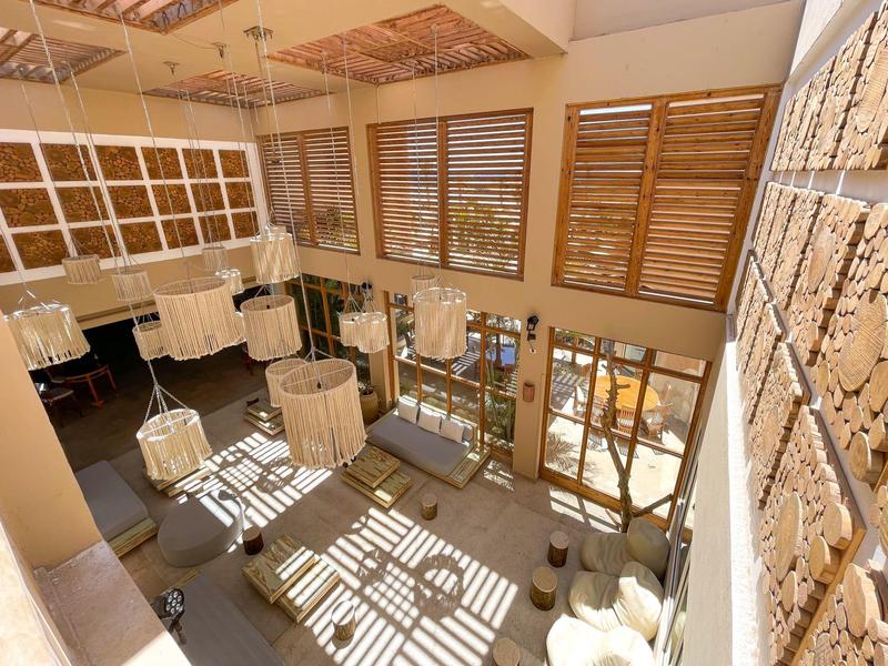 Großer Raum mit viel Tageslicht, Holzjalousien, hängenden Lampen und moderner Sitzgruppe.