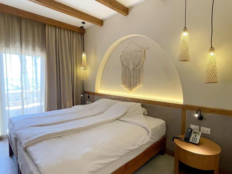 Schlafzimmer mit Doppelbett, Holzbalken, sanfter Beleuchtung und rundem Nachttisch mit Deko.