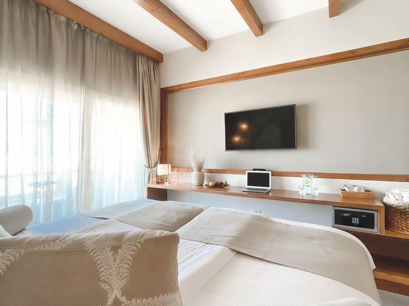 Modernes Wohnzimmer mit Holzbalken, heller Couch, großem Fenster und Fernseher an der Wand.