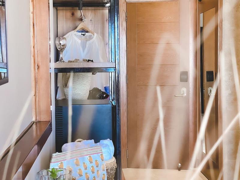 Kleiner Raum mit Holz- und Metallregal, Kleidungsstücken, Tür und Metallstange mit Vorhang.