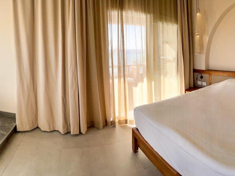 Helles Hotelzimmer mit Doppelbett, kleinem Esstisch und Blick auf die Landschaft durch große Fenster.