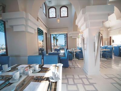 Area dell'hotel ben illuminata con sedie blu e tavoli bianchi che creano un'atmosfera elegante.