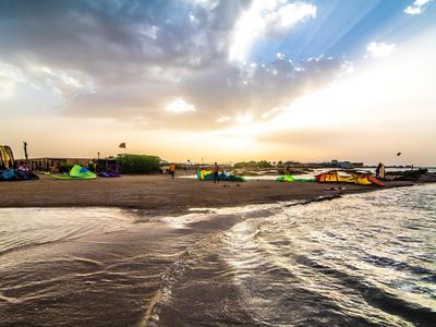 Ampia spiaggia sabbiosa al tramonto con sedie colorate e onde dolci.