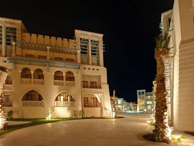 Nachtzicht op een verlichte hotelpad met palmbomen en traditionele architectuur.