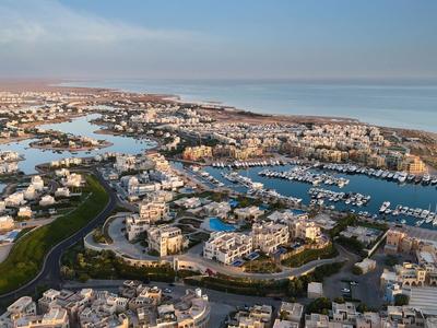 Luchtfoto van een kustresort met witte gebouwen en een jachthaven onder een blauwe lucht.