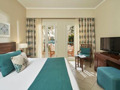 Chambre d'hôtel lumineuse avec lit double, accents bleu-vert et accès à la terrasse.