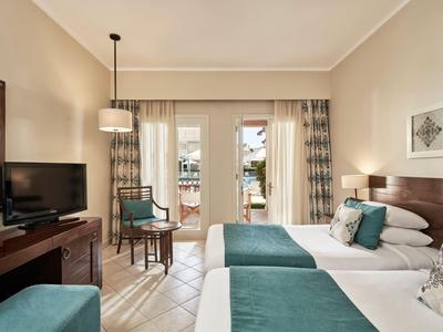 Chambre d'hôtel moderne avec deux lits, bureau, télévision et balcon donnant sur la piscine.