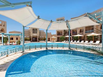 Piscina dell'hotel con tende da sole e lettini sotto un cielo limpido.