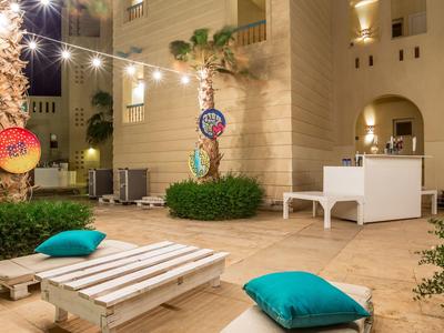 Buiten zitgedeelte met pallets, kussens, lichtslingers en palmbomen in een hotel binnenplaats.