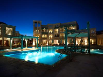 Area piscina dell'hotel illuminata con posti a sedere e edifici di notte.