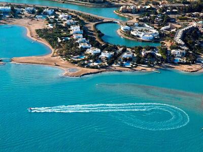Veduta aerea di una città costiera con acqua turchese e una barca che fa un giro ad anello.
