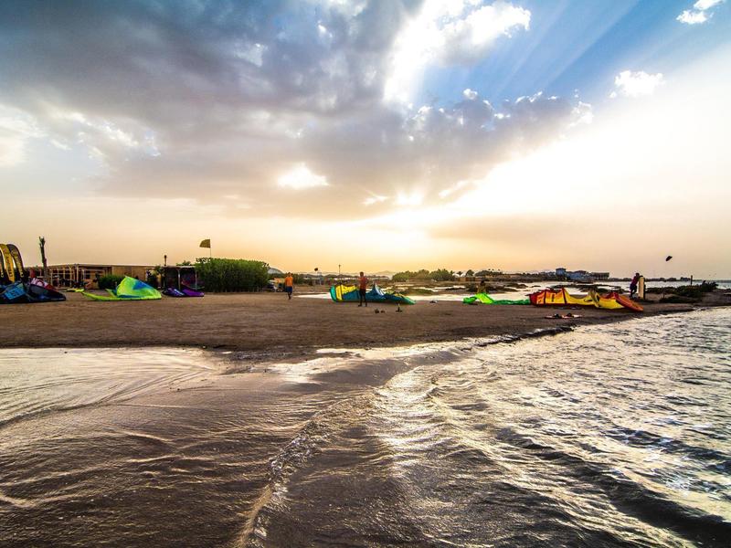 Zonsondergang boven een zandstrand met kleurrijke kites en kalme zee golven.