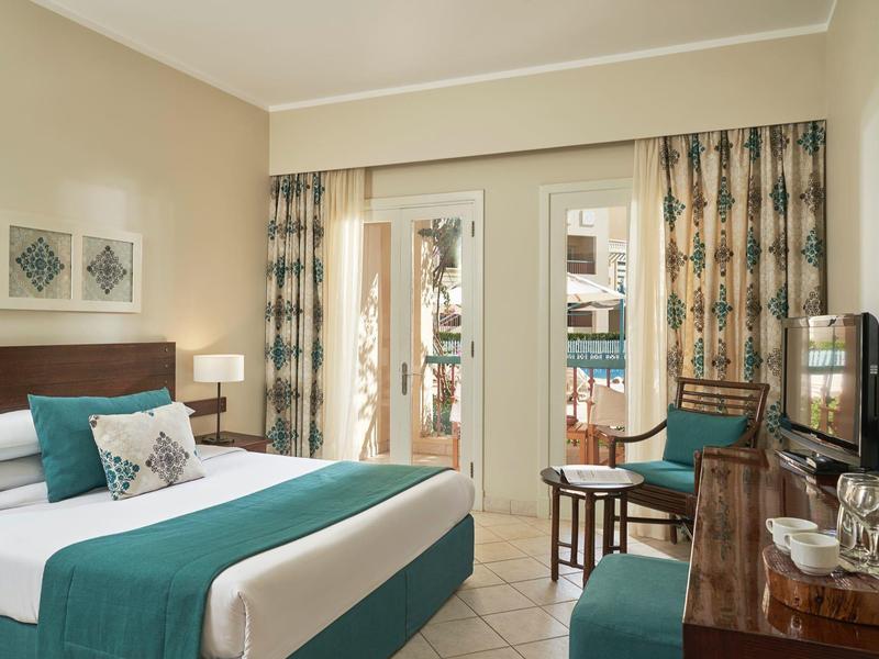 Hotelkamer met groot bed, turkooizen accenten en balkon met uitzicht op een binnenplaats.