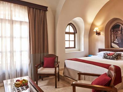 Chambre d'hôtel confortable avec lit double, chaises et lumière naturelle à travers les fenêtres.