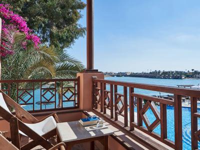 Balcon avec chaises longues donnant sur une piscine bleue et des palmiers sous un ciel clair.