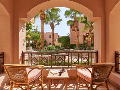 Balcon avec deux chaises en osier et une table donnant sur un jardin d'hôtel avec des palmiers.