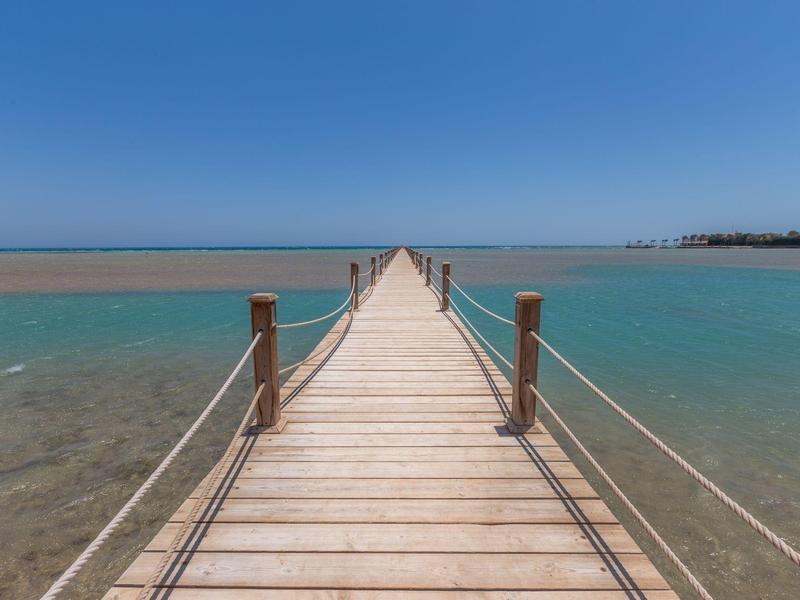 Jetée en bois s'étendant sur une eau turquoise claire sous un ciel bleu clair.