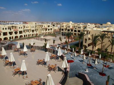 Vakantiehotel met zwembad, ligstoelen en parasols onder een blauwe lucht.