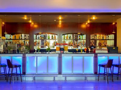 Area bar moderna in hotel con bancone illuminato di blu e sgabelli alti in un ambiente accogliente.