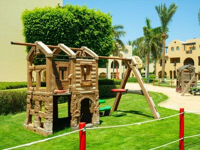 Area giochi con casette di legno e altalene davanti a edifici dell'hotel con cielo sereno.
