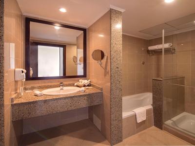 Helles Badezimmer mit großem Spiegel, Waschtisch, Glas-Duschkabine und beigen Fliesen.