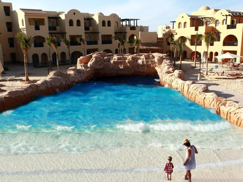 Hotel mit künstlichem Pool, umgeben von Felsen und mehrstöckigen Gebäuden in hellem Sandton.