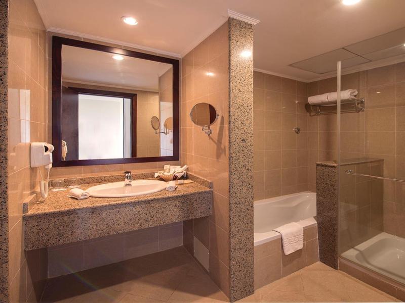 Helles Badezimmer mit großem Spiegel, Waschtisch, Glas-Duschkabine und beigen Fliesen.