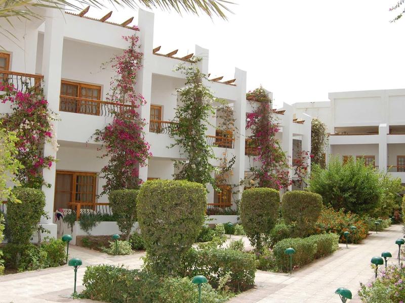 Bâtiment d'hôtel avec murs blancs, balcons et jardins verts bien entretenus.