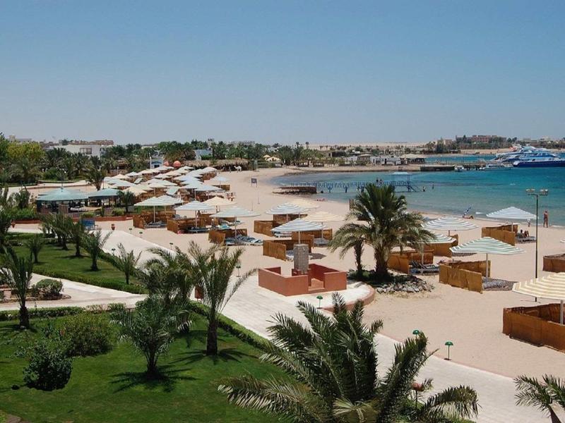 Plage avec sable blanc, palmiers et parasols le long d'une côte bleue.