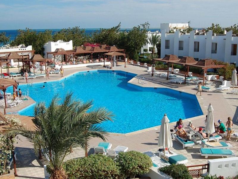 Grande piscine extérieure avec chaises longues et bâtiments blancs en arrière-plan au bord de la mer.
